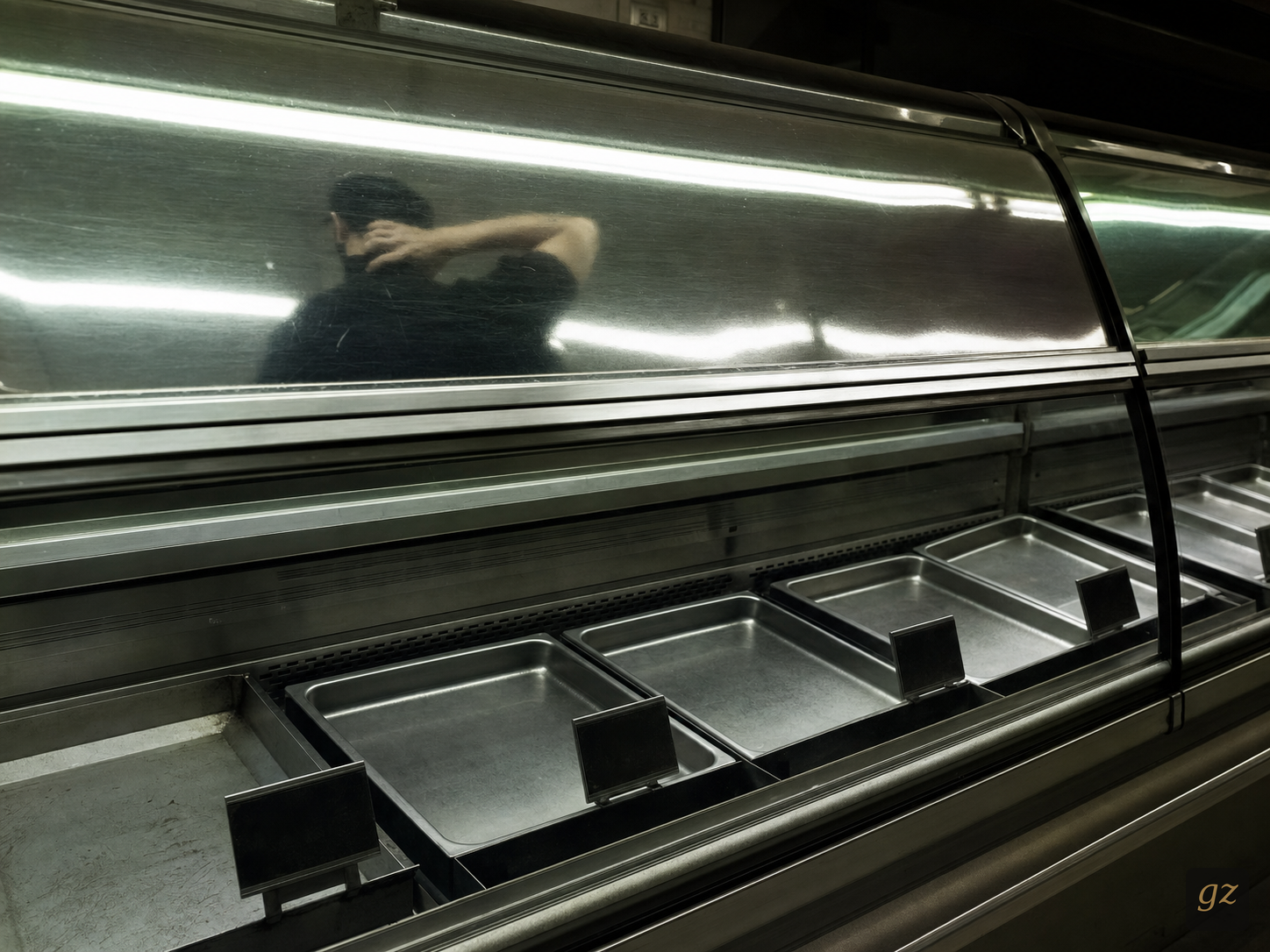 A deli case reflection. A worker reaches for the back of their neck.