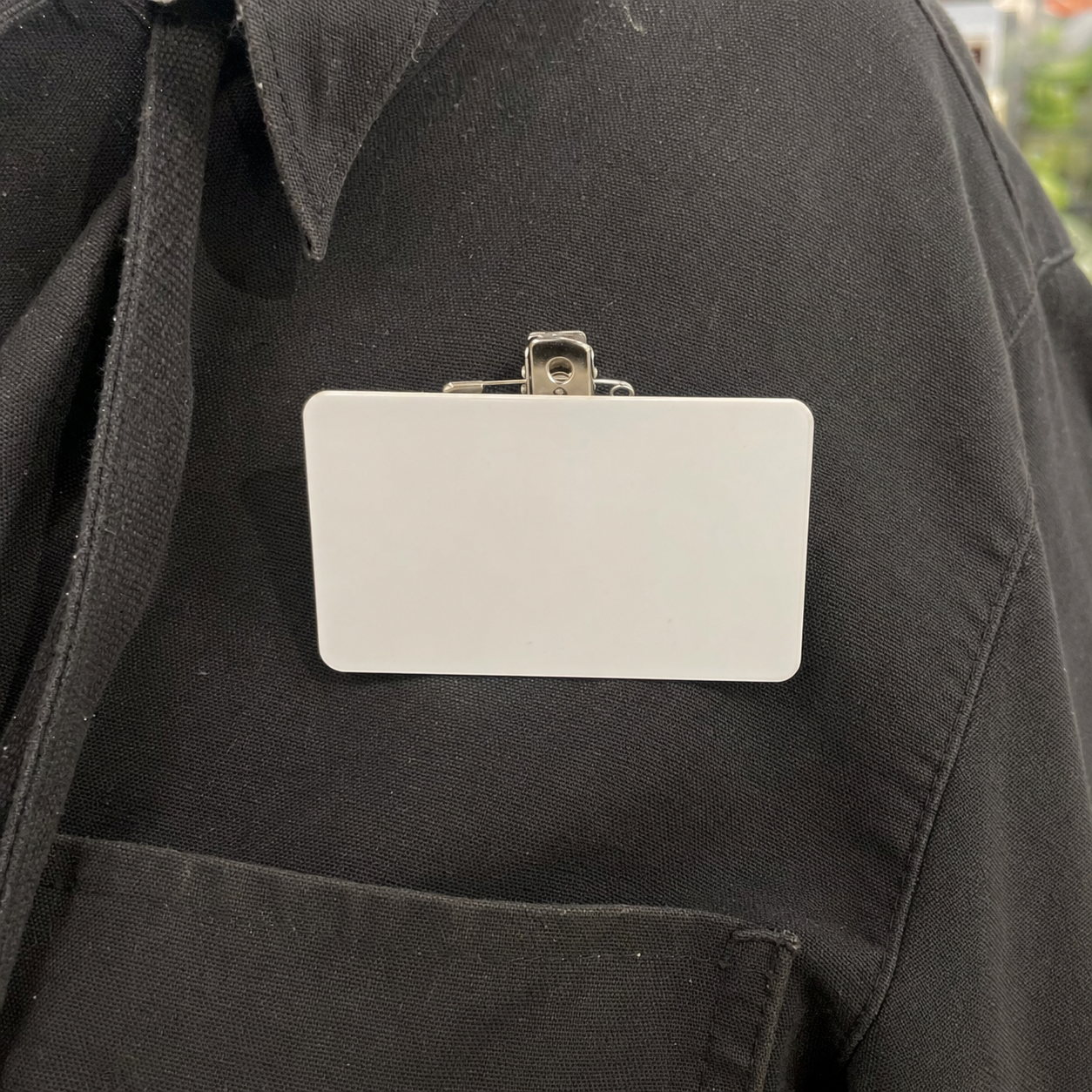 A blank white name tag clipped to a black shirt, printed with the name GREYGRAY.