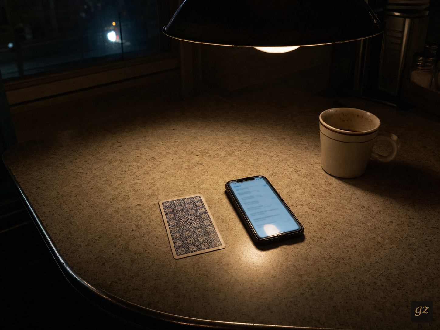 A single tarot card face up beside a phone showing an app. One pendant lamp lights the table.